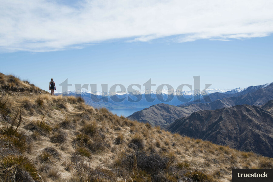 Female adult standing on mountain peak overlooking the mountain ranges and lake