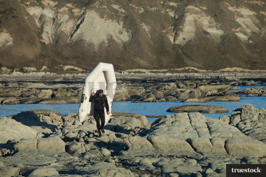 Male adult walking on the rocks carrying a dinghy boat back to shore