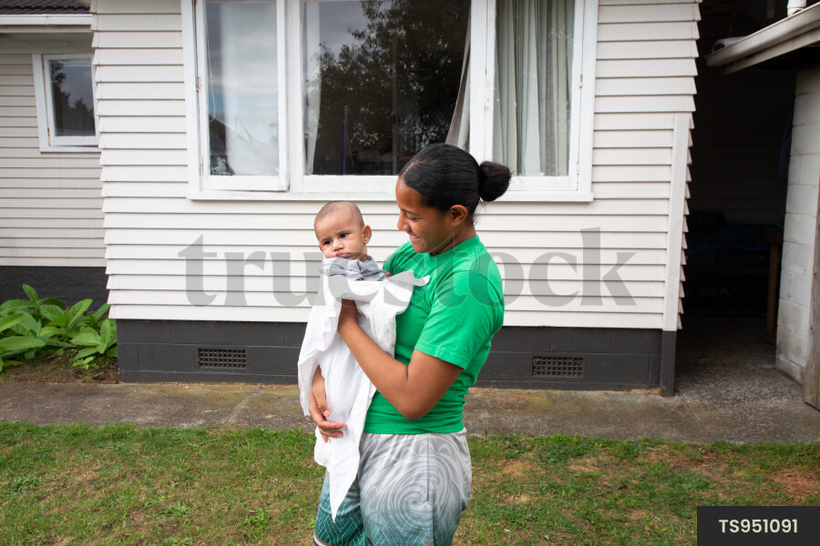 Tongan sister holding baby brother outside house