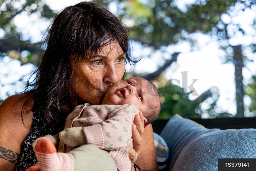 Grandmother kissing newborn granddaughter on sofa in living room