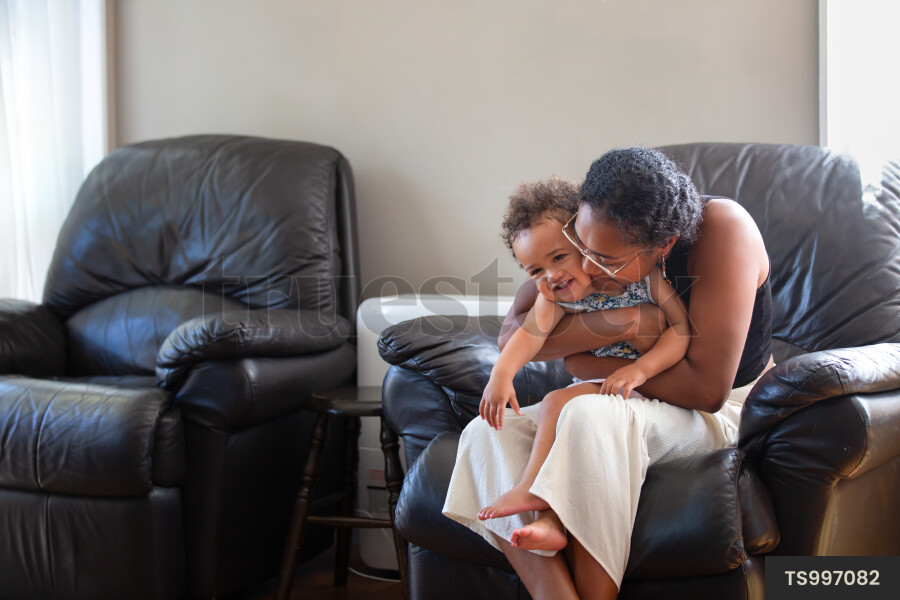 Mother kissing daughter on armchair in house